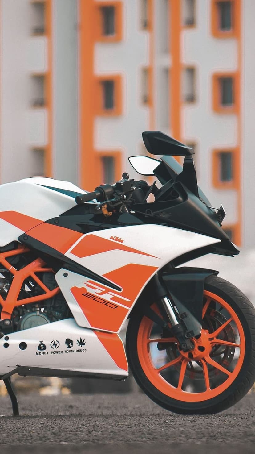 KTM RC 200 motorcycle with orange and white fairing parked outdoors against a blurred architectural background.
