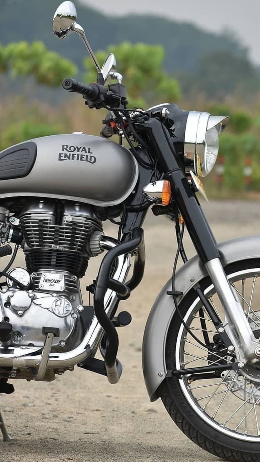 Royal Enfield Classic 350 motorcycle with a silver fuel tank, chrome engine, and disc brake on a blurred lawn.