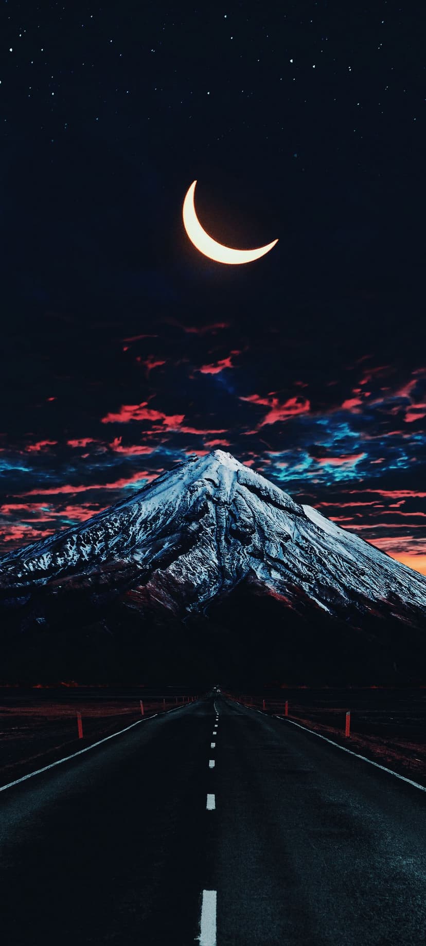 Snow-capped mountain peak looms over a dark asphalt road under a starry night sky with a glowing crescent moon.