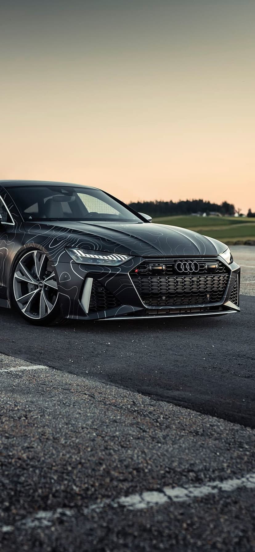 Audi RS7 with a topographic map wrap parked on an asphalt road during a vibrant golden hour sunset sky.