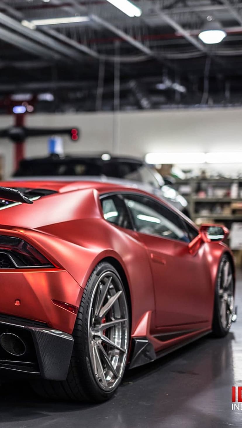 Matte red Lamborghini Huracan with silver wheels parked in a bright garage for a mobile device screen display.
