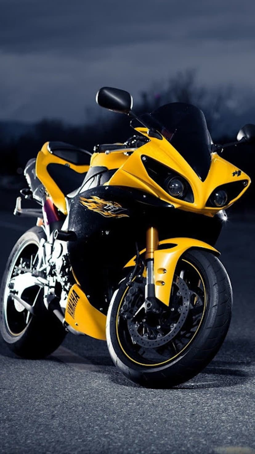 Yellow Yamaha sportbike with glowing dual headlights and sharp front fairing on dark asphalt under a gray sky.