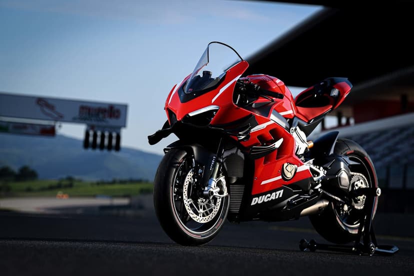 Red Ducati Superleggera V4 motorcycle with carbon fiber winglets parked on a sunlit asphalt racetrack.