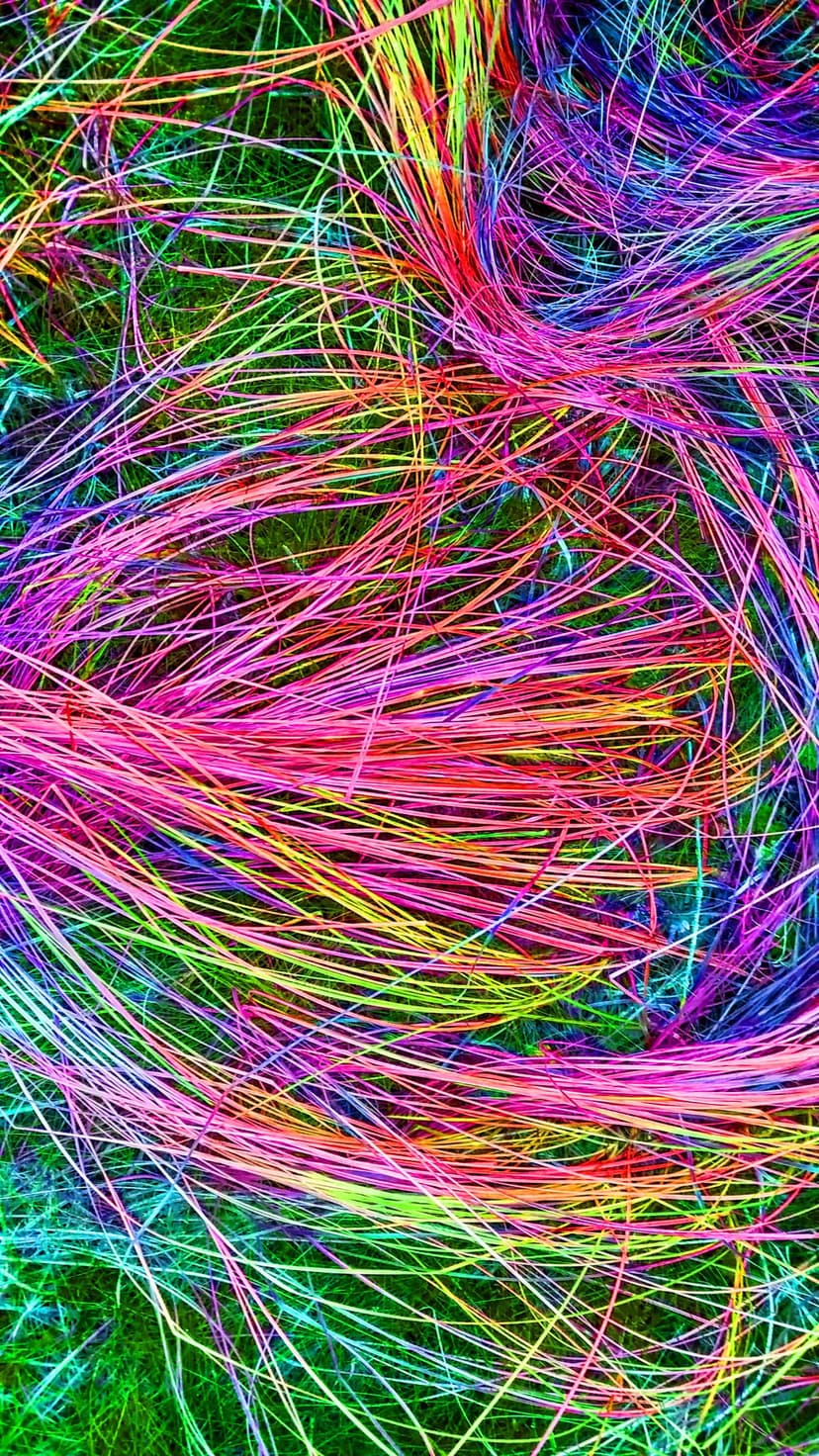 Neon pink, green, and blue threads tangle in a dense web over a dark textured surface in a macro perspective.