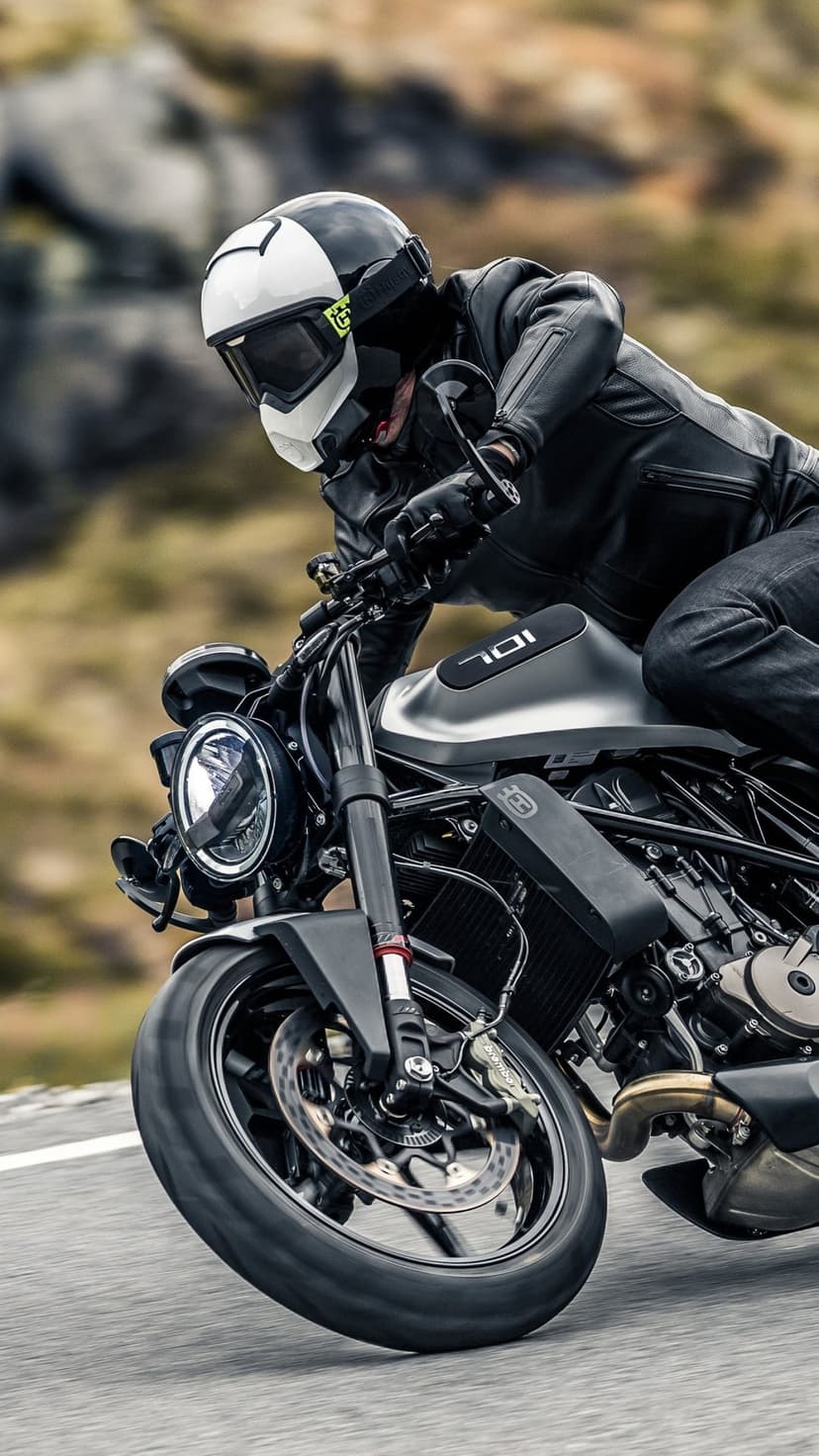 Husqvarna 701 motorcycle leaning into a turn with a rider in black leathers and a white helmet on a road.