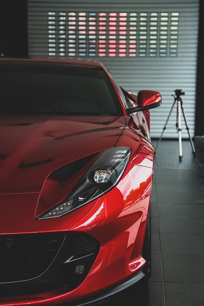Red Ferrari front headlight and aerodynamic fender reflecting studio lights in a professional photoshoot setting.
