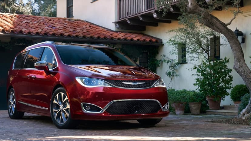 Metallic red Chrysler Pacifica minivan parked in a cobblestone driveway before a white Mediterranean house.