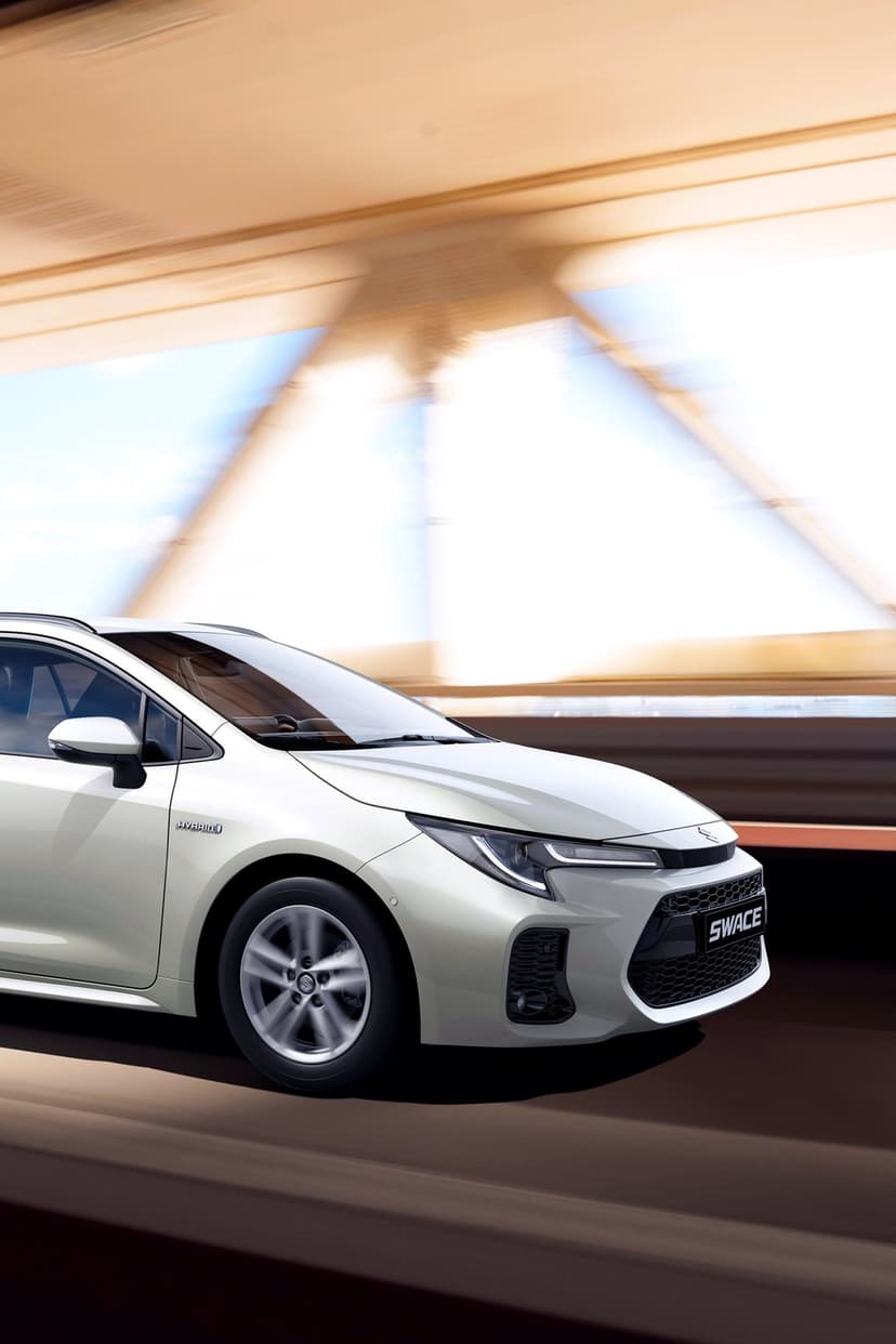 White Suzuki Swace car driving on a bridge with motion blur on wheels and background in bright daylight.