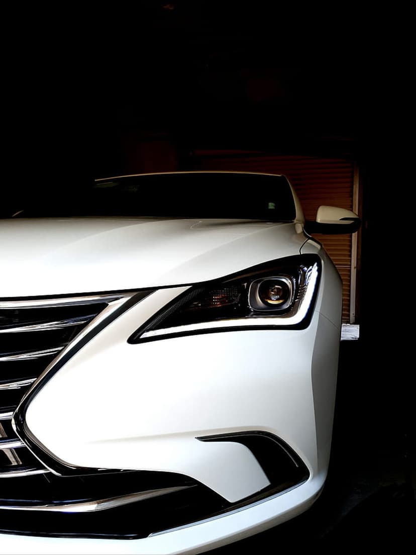 White Lexus LED headlight and chrome spindle grille captured from a low angle against a dark background.
