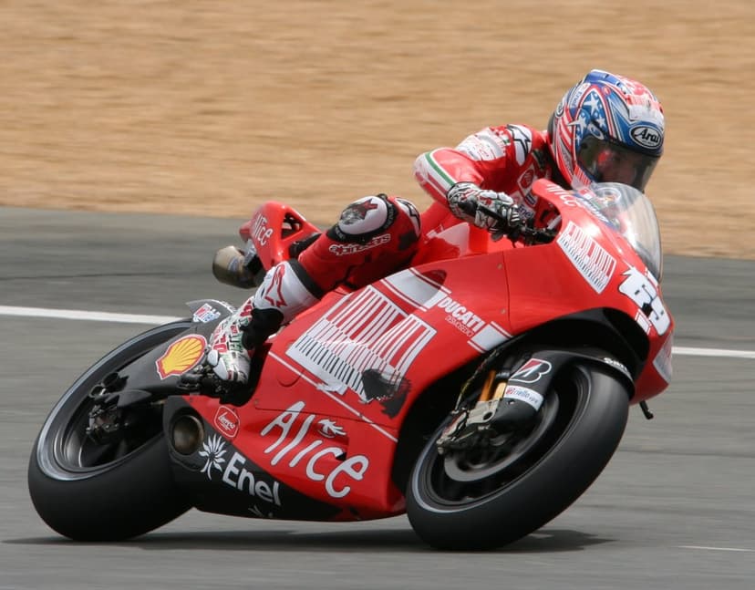 Professional motorcycle racer on a red Ducati leans into a racetrack corner during a high-speed sports event.