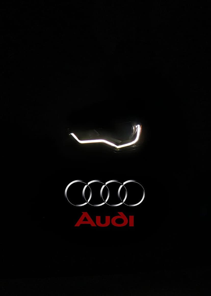 Audi four rings logo in silver below a white LED headlight with red brand lettering on a black background.