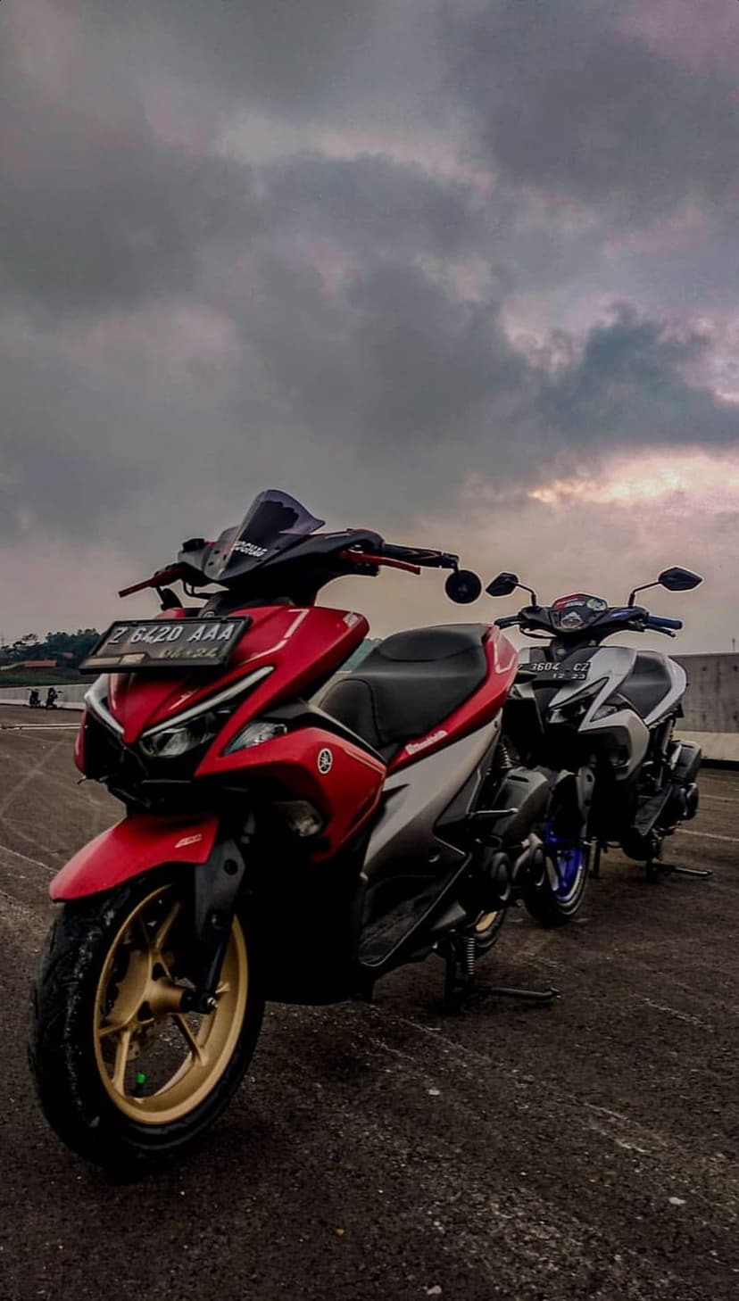 Red and white Yamaha scooter with gold rims parked beside a black and white model under a moody overcast sky.