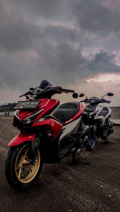 Two Yamaha scooters parked outdoors under cloudy sky