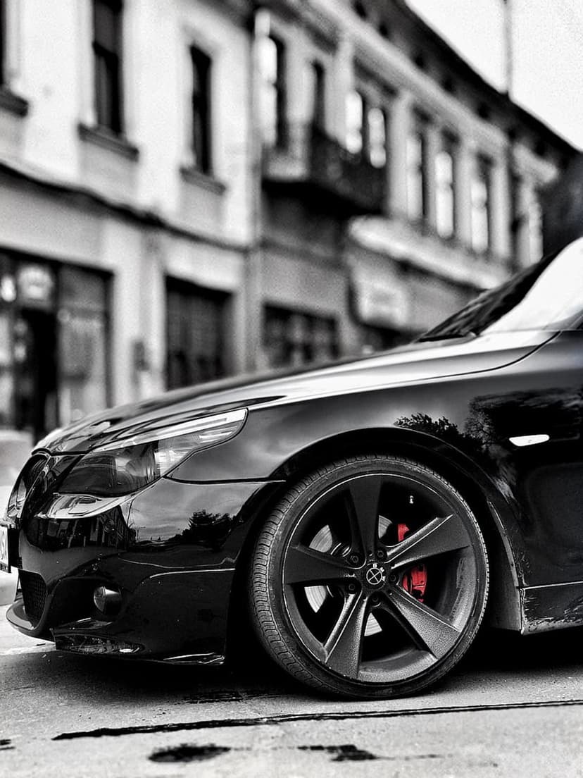 BMW alloy wheel with a bright red brake caliper parked on a city street with a blurred urban background.