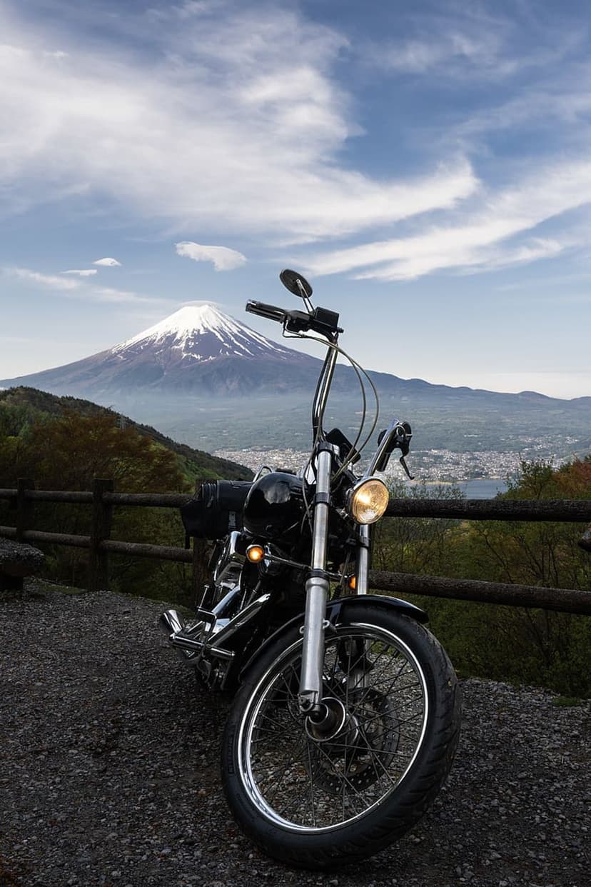 Black cruiser motorcycle parked on a gravel path facing the snow-capped Mount Fuji under a clear blue sky.