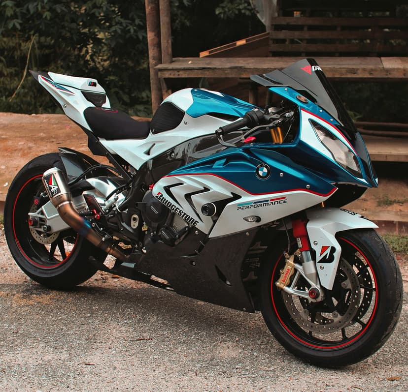 BMW S1000RR sportbike with white and blue fairings parked on gravel in front of a rustic wooden structure.