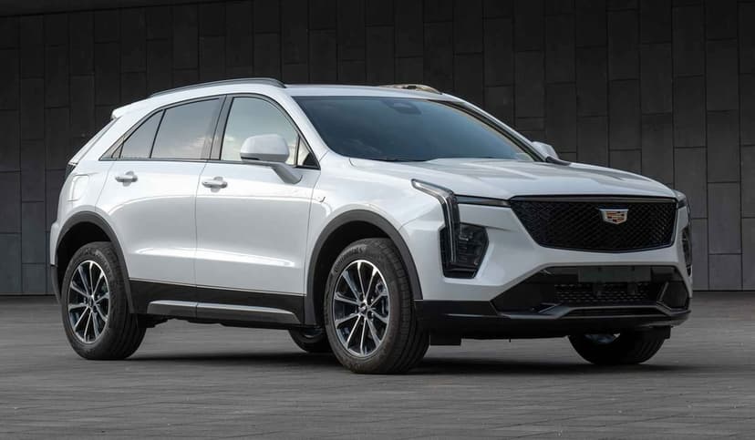 White luxury Cadillac SUV parked in front of a dark gray slate wall with sleek LED headlights and alloy wheels.