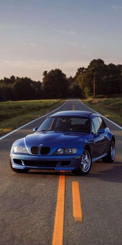Blue BMW M Coupe drives down scenic country road