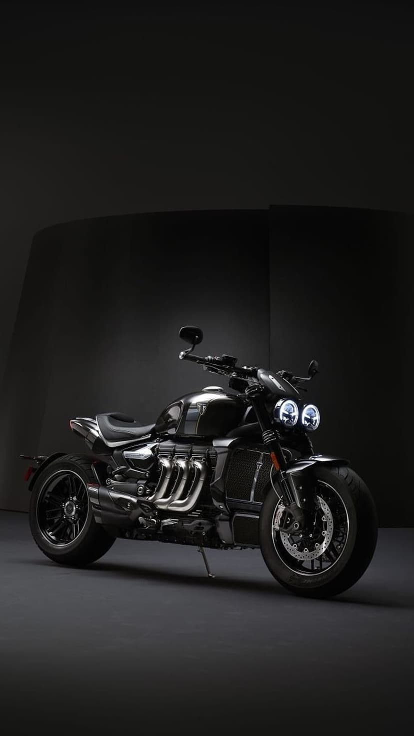 Triumph Rocket 3 motorcycle in a dark studio with dramatic rim lighting on its black frame and triple exhausts.