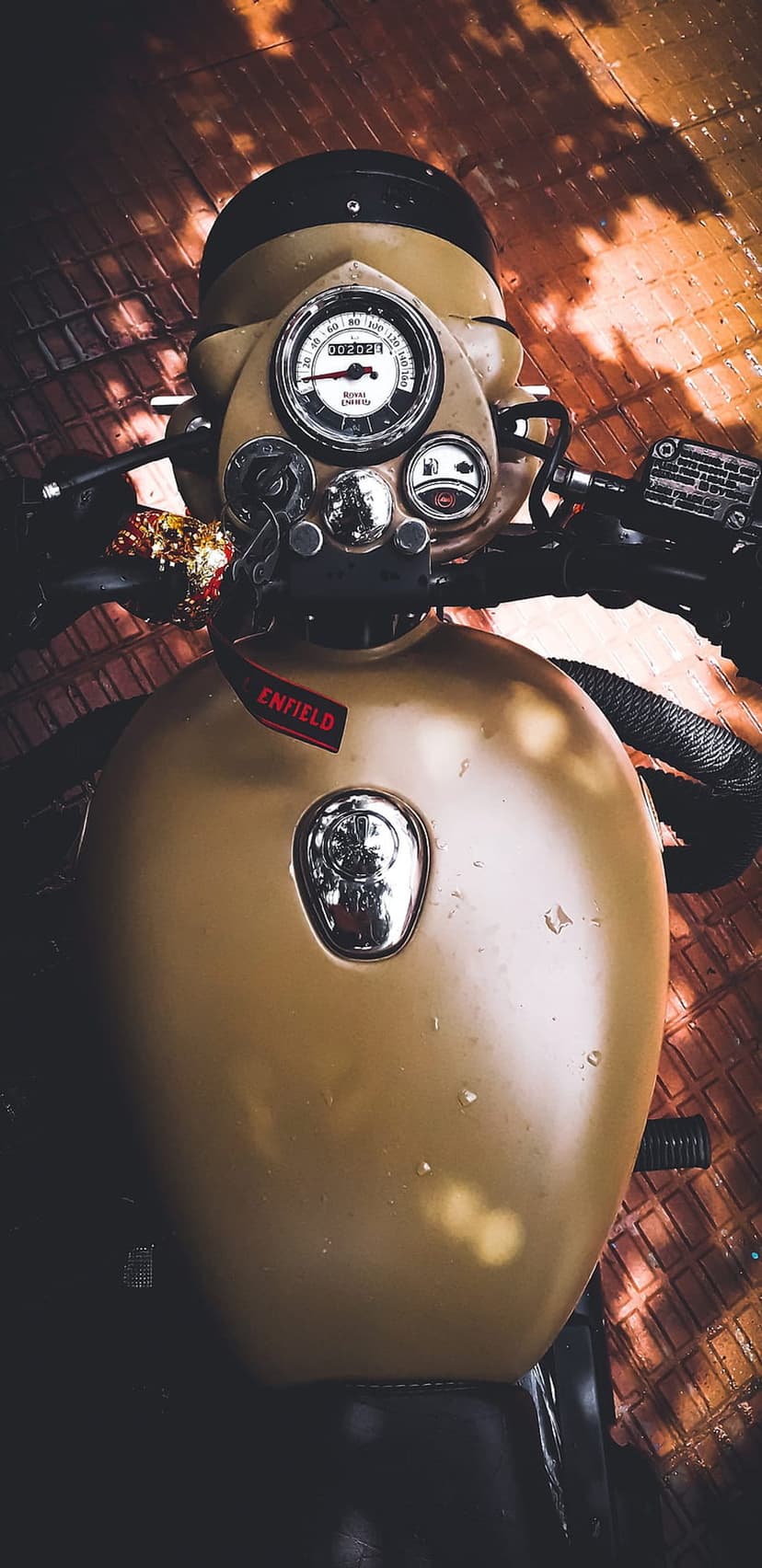 Analog speedometer and tan fuel tank on a vintage Royal Enfield motorcycle with polished chrome handlebars.