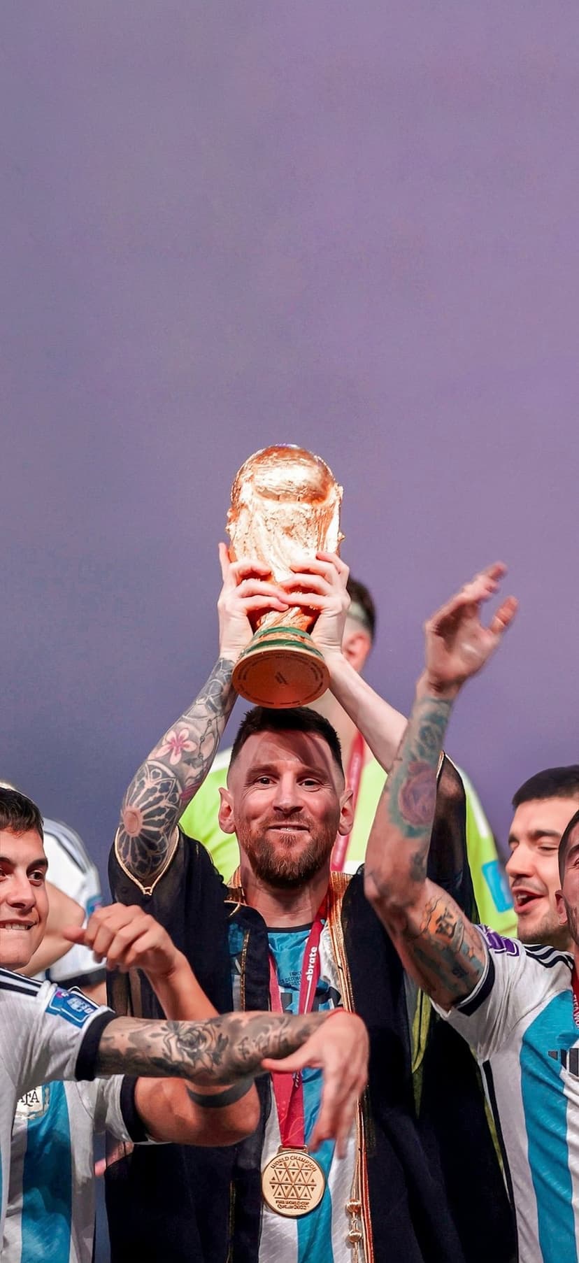 Lionel Messi lifts the gold FIFA World Cup trophy while wearing a black bisht robe and showing his arm tattoos.