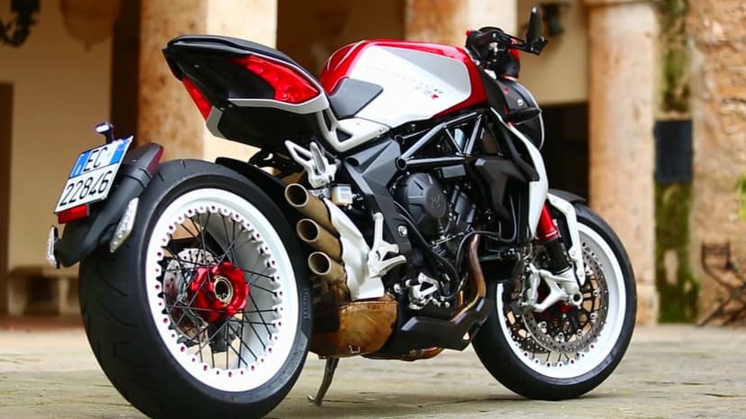 Rear view of a red and white MV Agusta Dragster motorcycle with triple exhausts on a stone walkway.