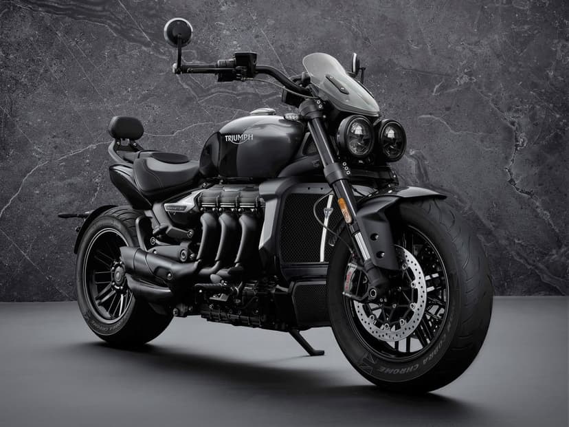 Black Triumph Rocket 3 GT motorcycle with dual headlights against a dark textured marble wall background.