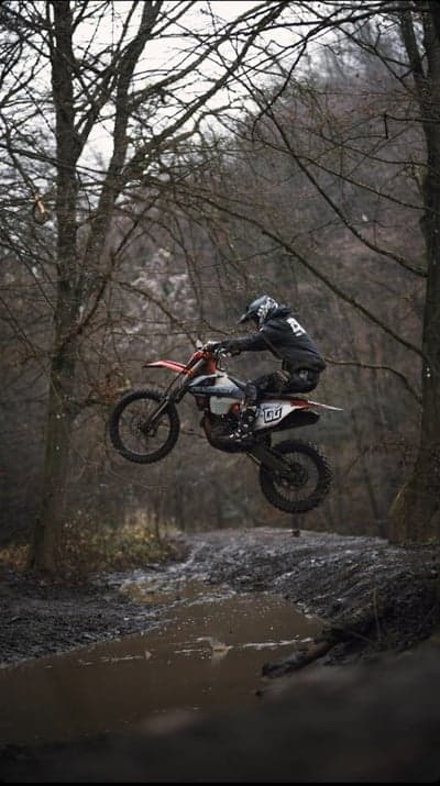 Motocross rider soars through muddy forest during jump