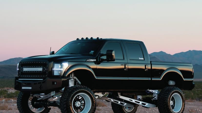 Lifted black custom Ford truck with oversized wheels and white suspension in a desert during a golden hour sunset.
