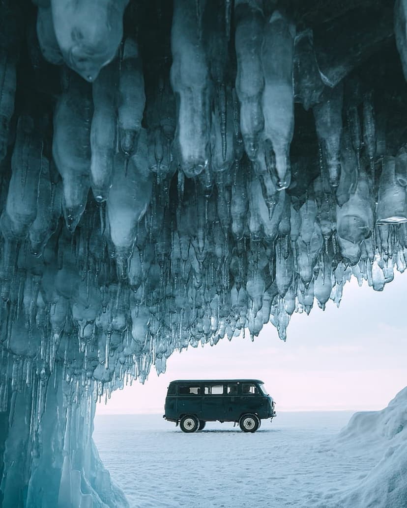 Dark green vintage van parked on a frozen lake surface next to massive blue icicles and an icy overhang.