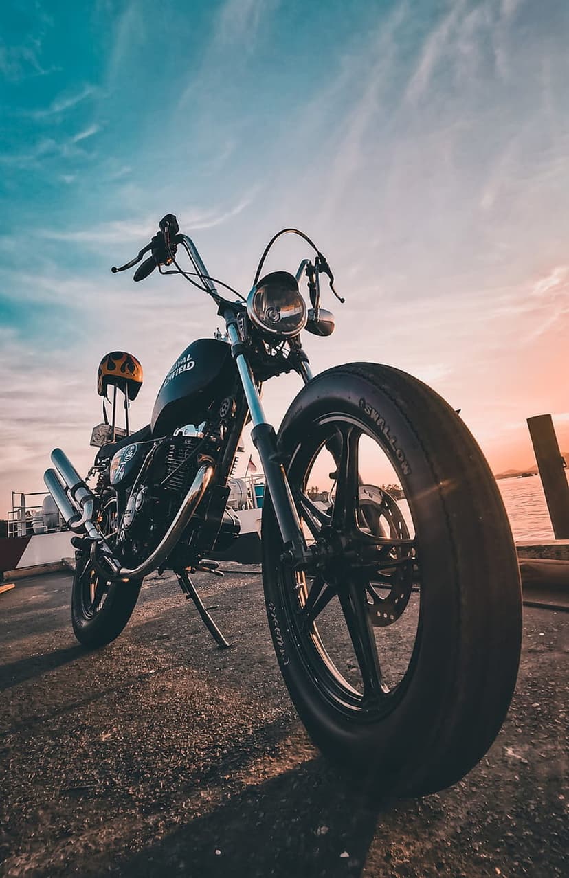 Black motorcycle with a yellow helmet sits on a pier during a vibrant orange and blue sunset over the ocean.