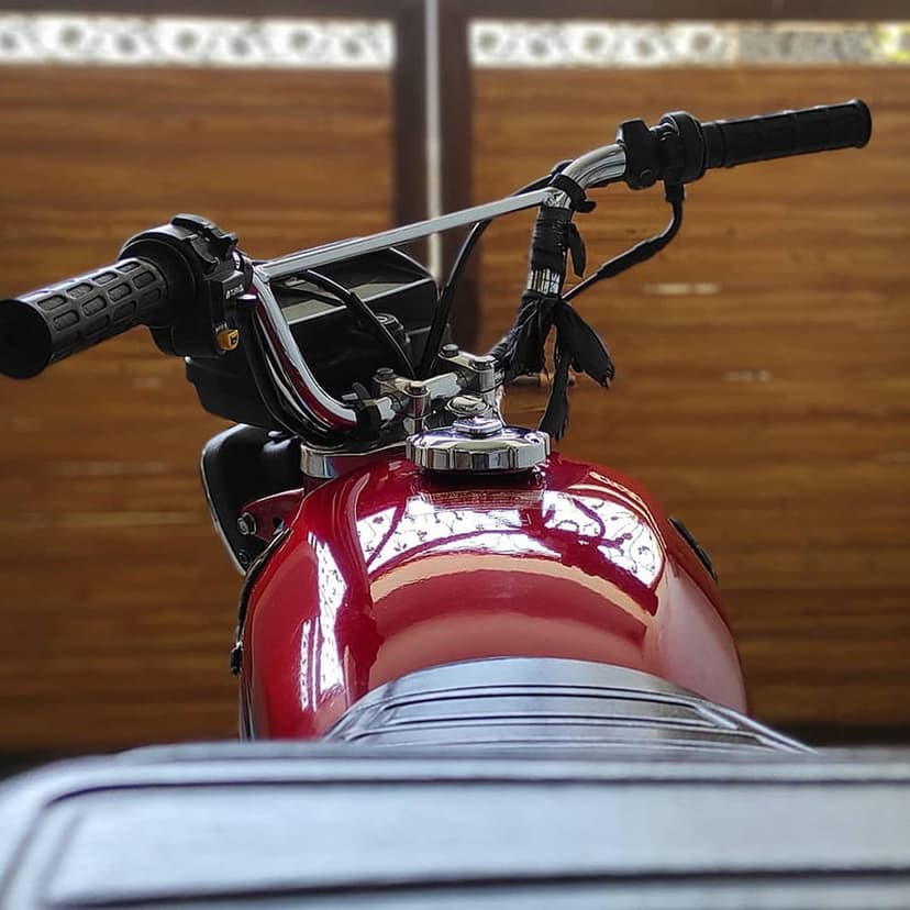 Vintage red motorcycle fuel tank and chrome handlebars with black grips against a blurred wood background.