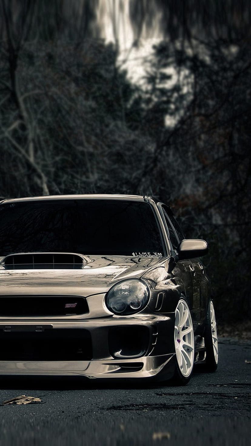 Subaru WRX STI featuring white rims parked on a wet forest road under soft, ethereal light filtering through trees.