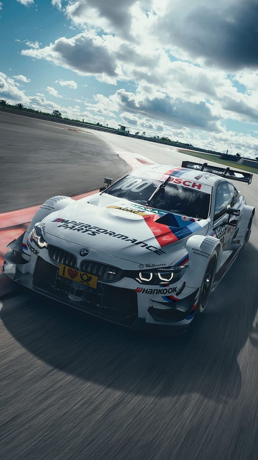 White BMW M Performance race car cornering a track under dramatic clouds with Bosch and ADAC sponsorship logos.