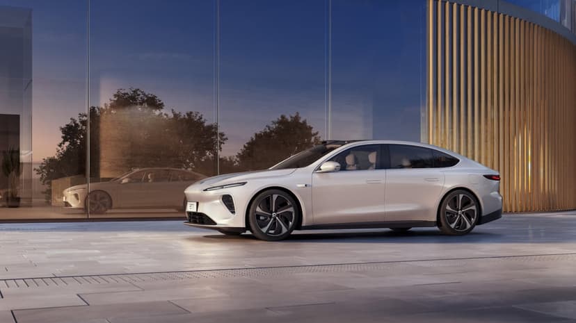 Sleek white electric sedan parked before a glass building with warm sunset reflections on its surface.