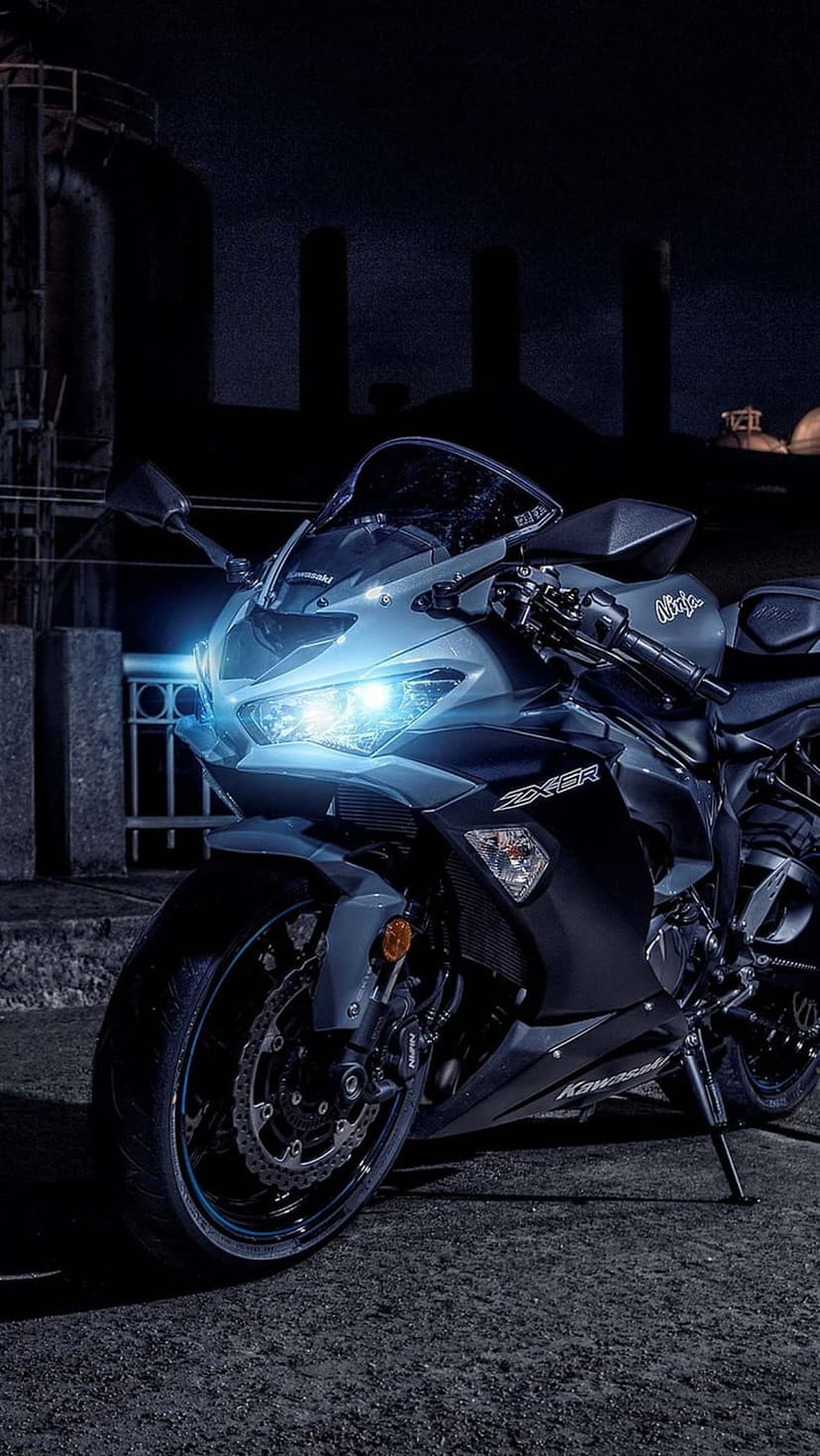 Kawasaki Ninja ZX-6R motorcycle with illuminated blue headlights parked in a dark industrial zone at night.