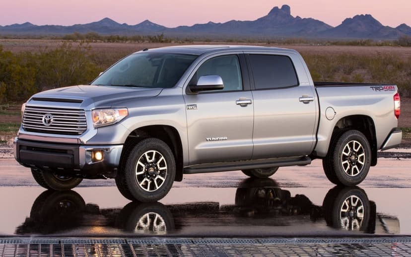 Silver Toyota Tundra pickup truck reflecting on wet pavement in a desert landscape during a soft pink sunset.