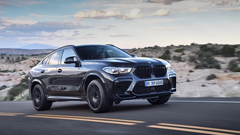 Black BMW X6 M Competition driving on a desert road with motion blur under a sunset sky during golden hour.