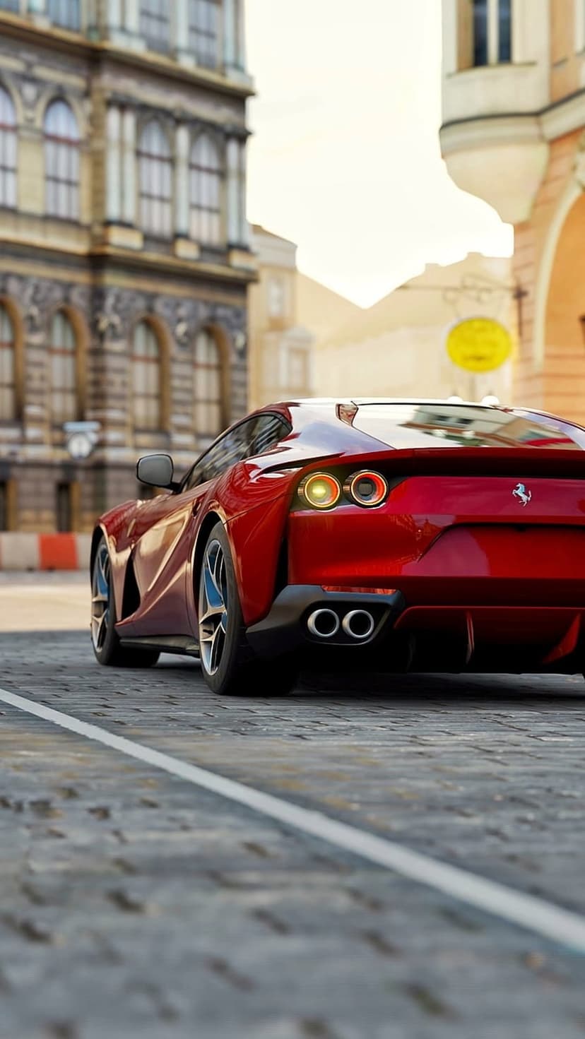 Red Ferrari rear profile driving on a cobblestone road past historic European buildings in soft light.