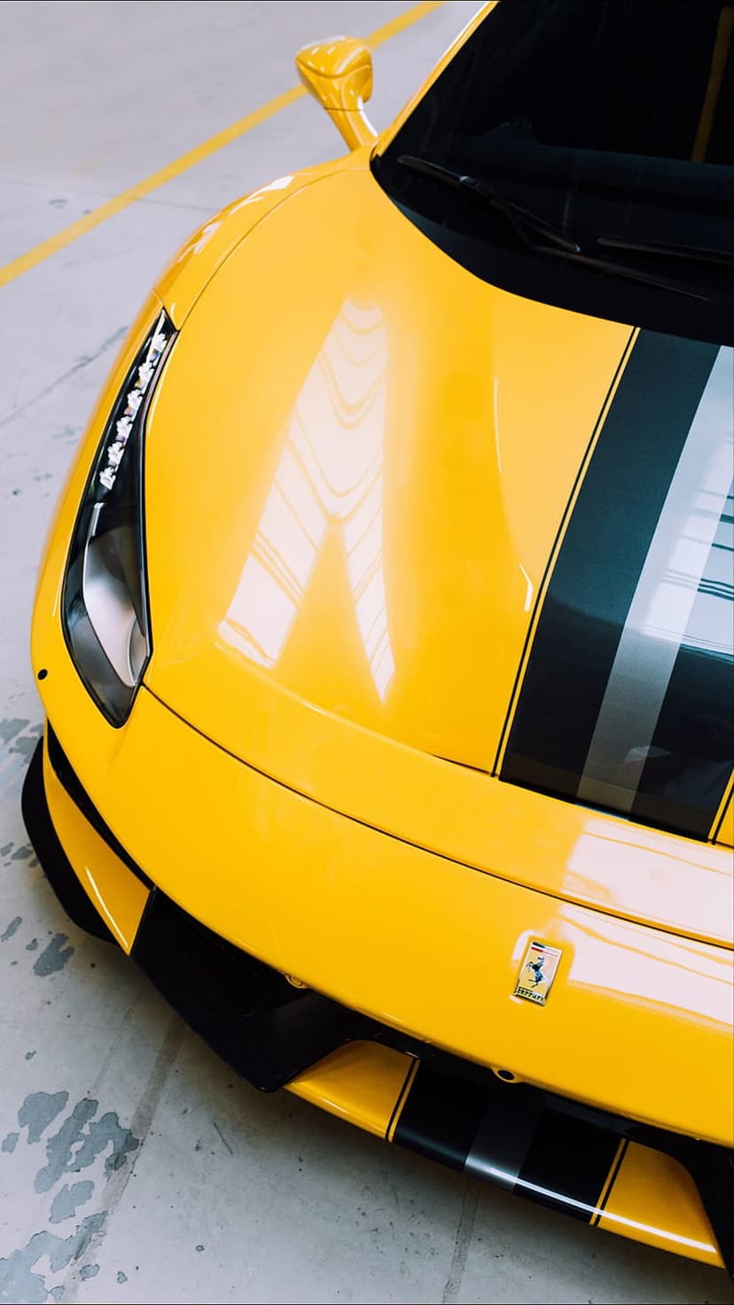 Yellow Ferrari front bumper with racing stripes and emblem on a concrete floor in a dark garage setting.