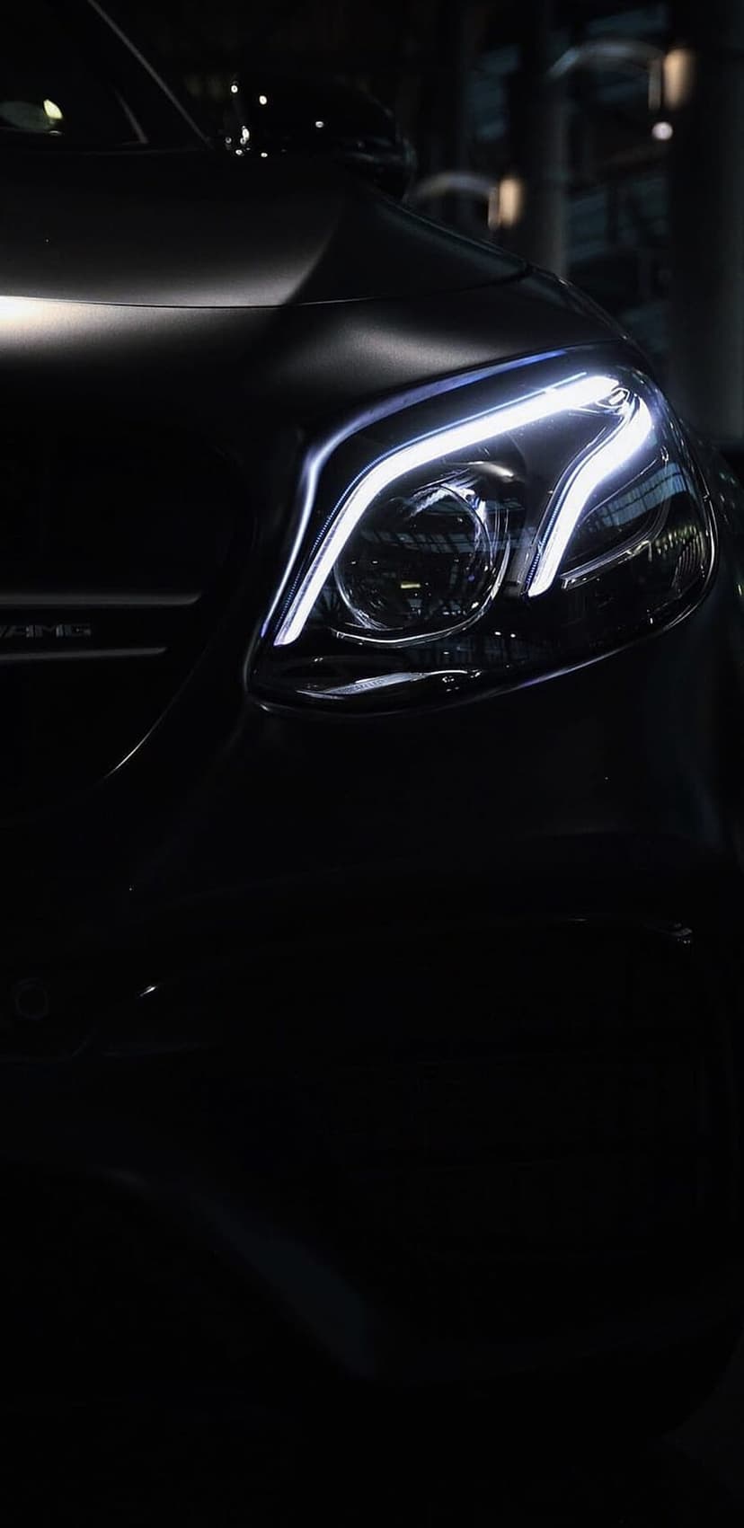 White LED headlight and AMG grille on a dark metallic car at night with sharp light reflections on the body.