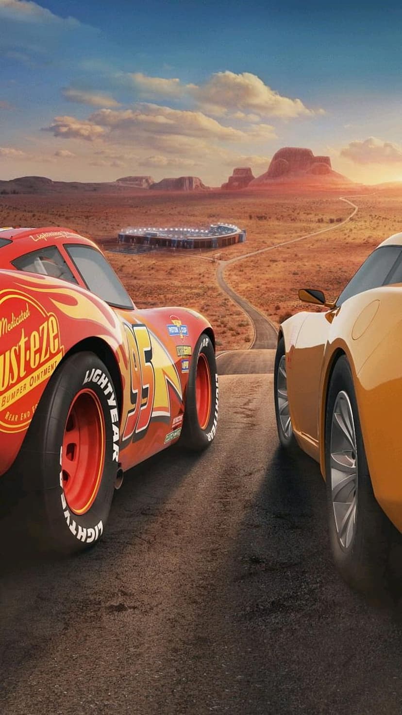 Lightning McQueen and a yellow sports car drive toward a stadium on a desert road under a golden sunset sky.