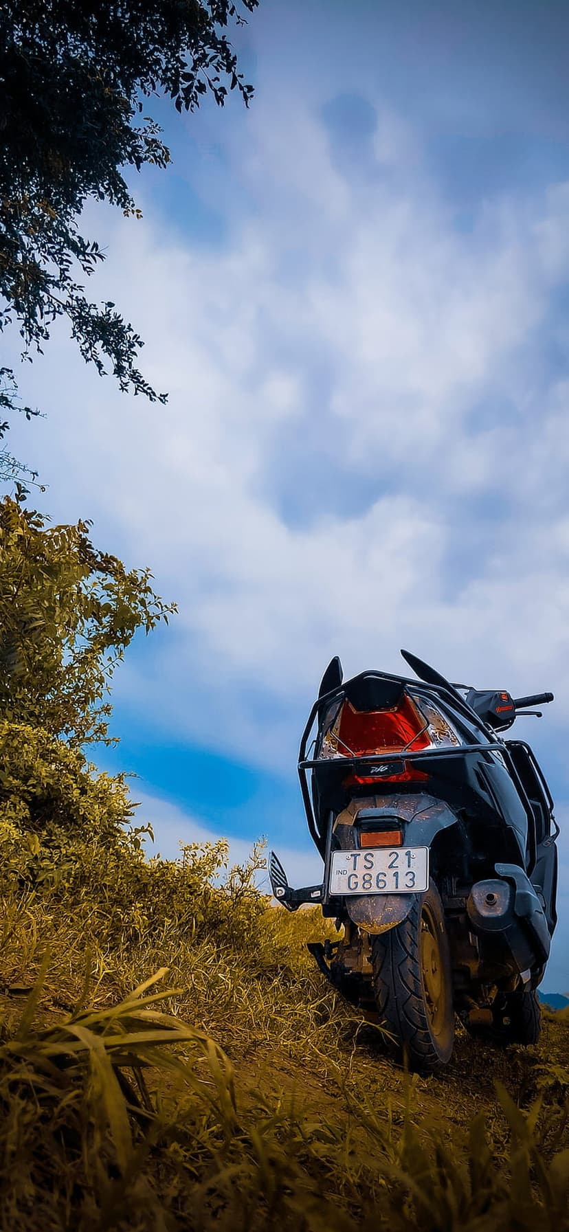 Black motorcycle parked on a yellow-green grassy slope under a sky filled with heavy, textured clouds.
