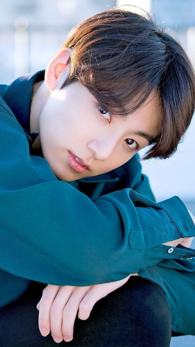Jungkook from BTS wearing a teal button-up shirt with arms crossed, featuring soft lighting and dark messy hair.