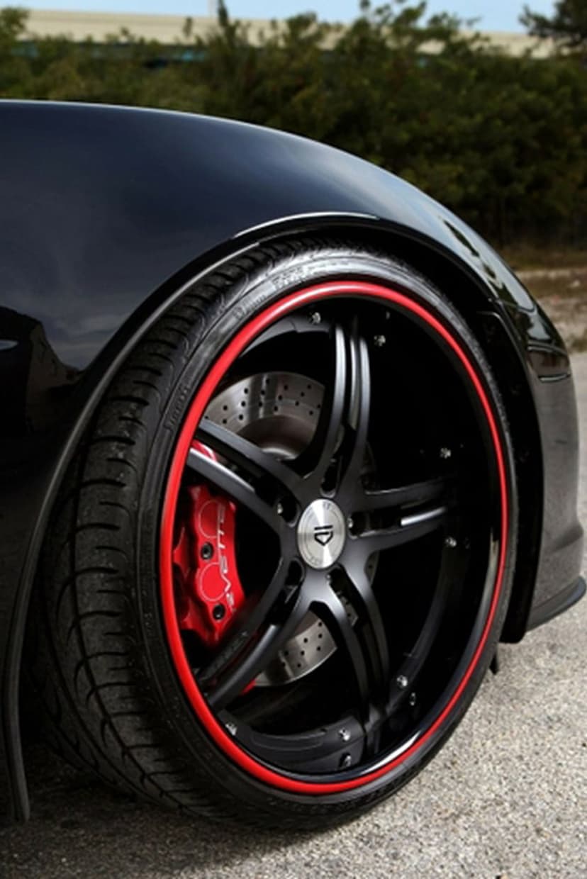 Black multi-spoke car rim featuring a red outer lip and visible red brake caliper with drilled metallic rotors.