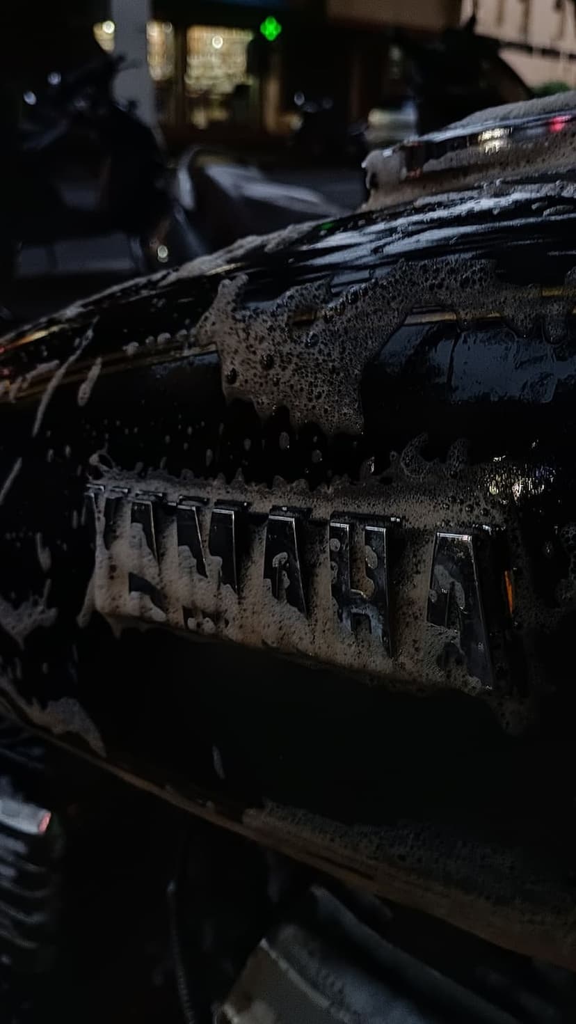 Yamaha chrome logo visible through thick white soap suds on a black motorcycle panel during a night wash.