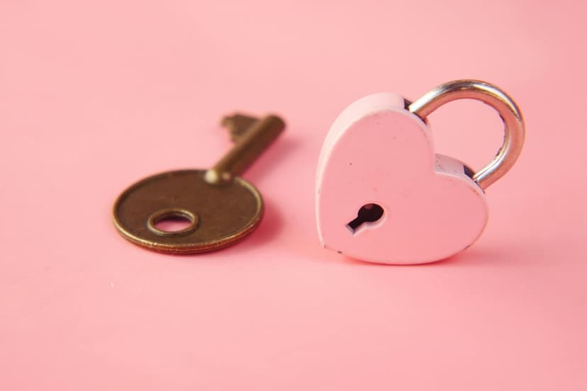 Pink heart-shaped padlock with a silver shackle beside an ornate brass key on a flat pastel pink surface.