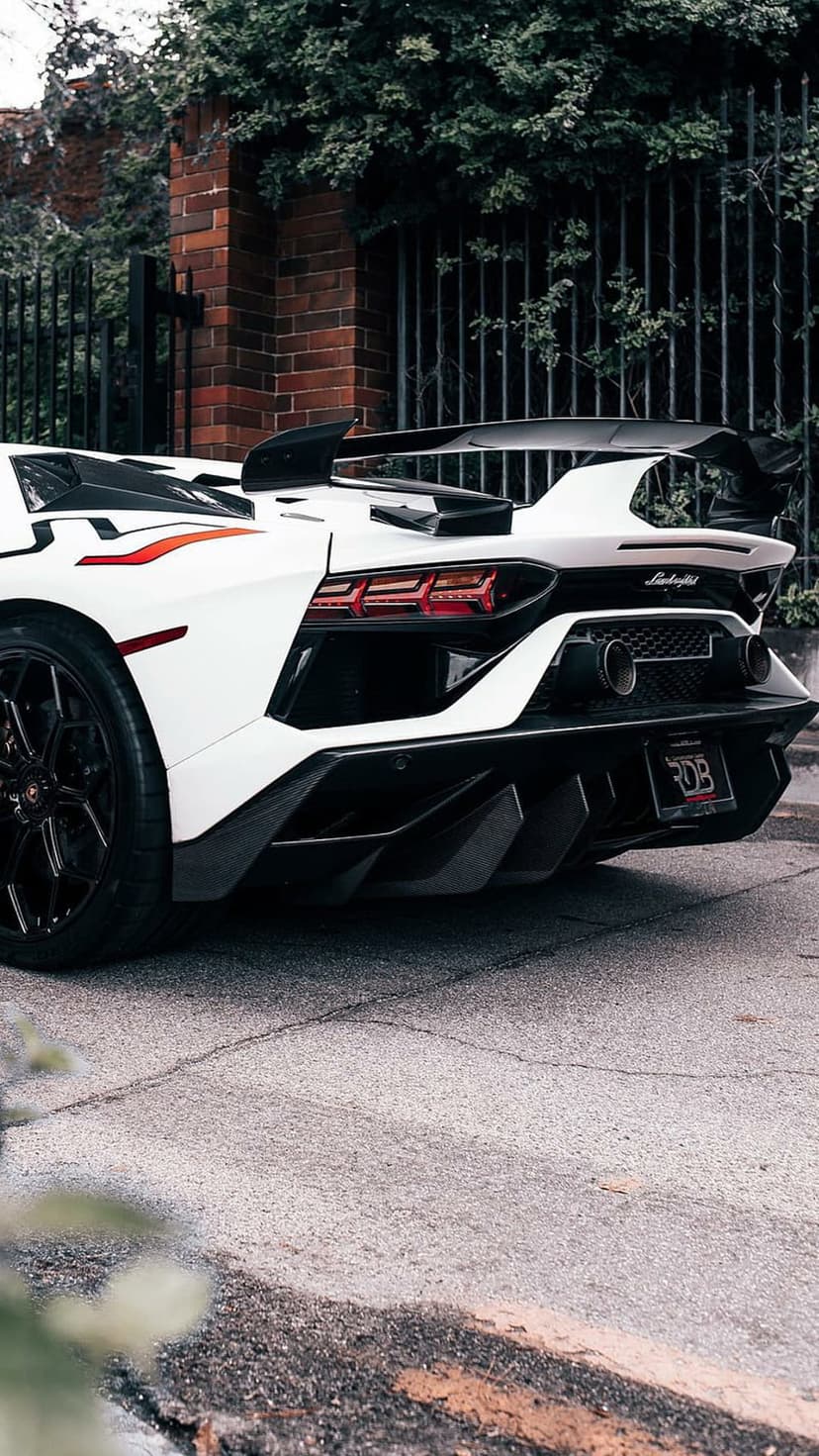 White Lamborghini Aventador SVJ rear view with a large wing, quad exhausts, and taillights on cracked asphalt.