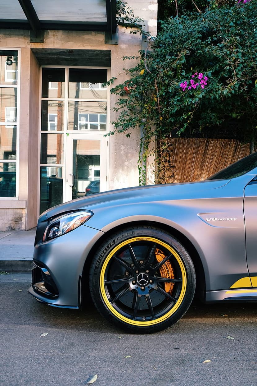 Mercedes-AMG sedan in gray with yellow brake calipers parked near green climbing vines with small pink flowers.