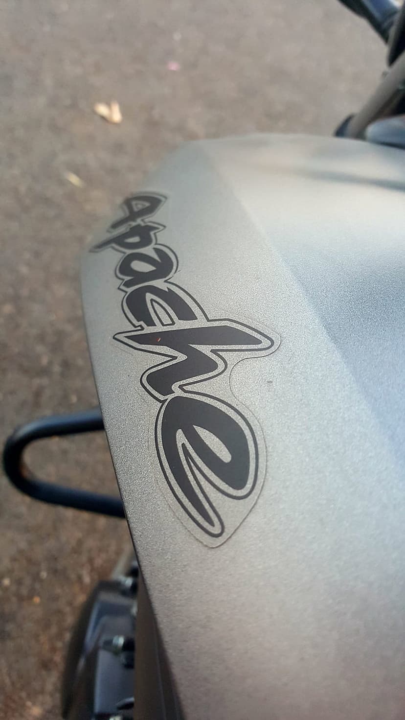 TVS Apache motorcycle fender with a matte grey finish and black logo displays a textured automotive surface.